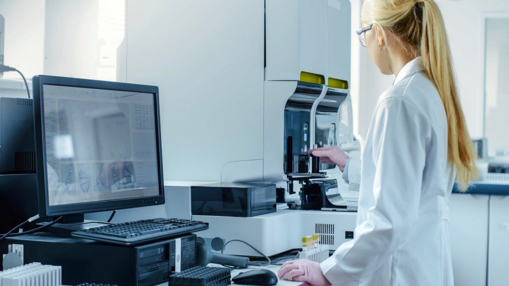 Female Research Scientist Working with Medical Analyzing Machine for Testing Tubes with Blood Sample. Scientist Works in Innovative Pharmaceutical Genetic Research Laboratory.
