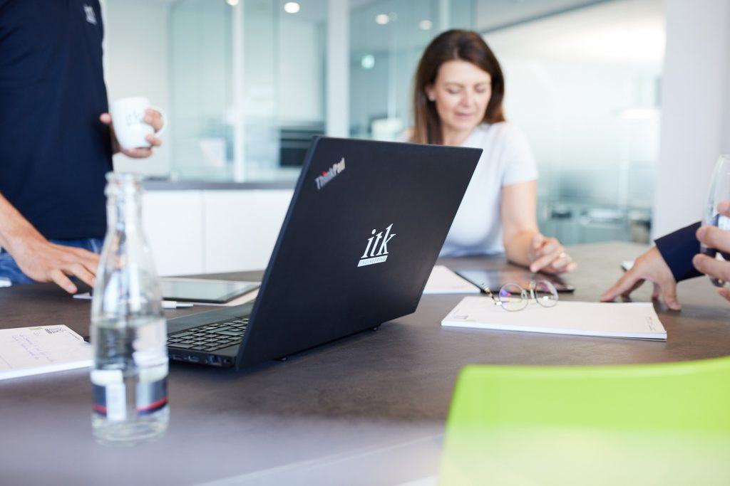 ITK Laptop auf einem Tisch mit ITK-Mitarbeiterin im Hintergrund