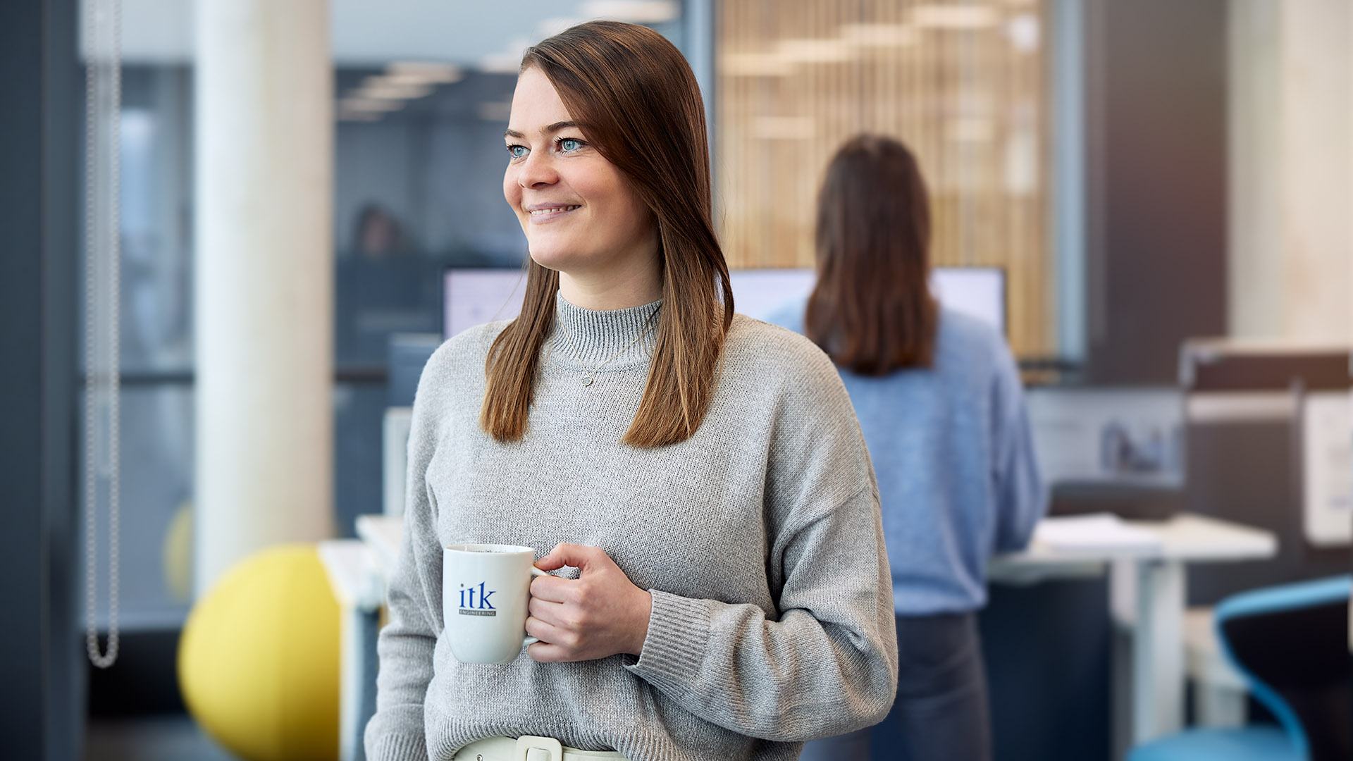 Eine ITK-Mitarbeiterin mitten im Büro und einer ITK-Tasse in der Hand