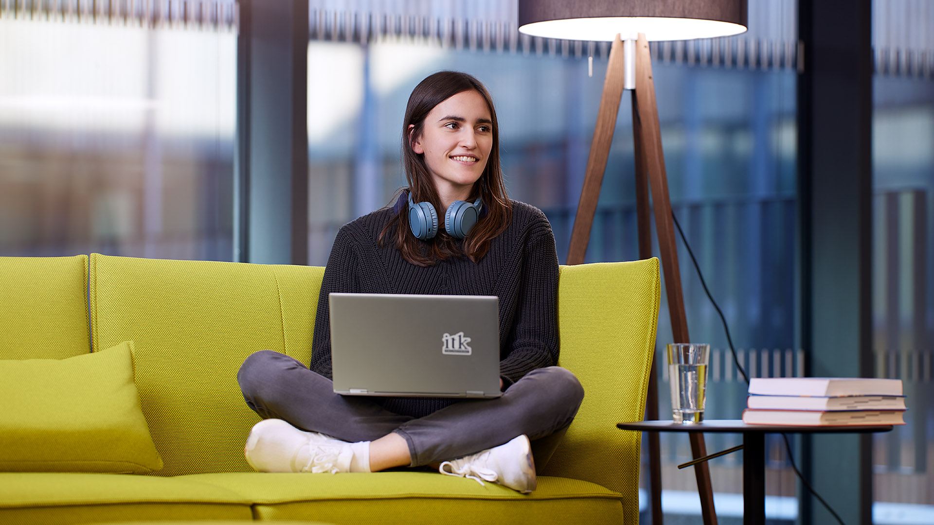 A young ITK student sitting cross-legged on a green sofa with a laptop