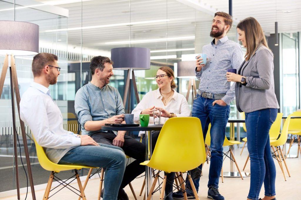 5 ITK-Mitarbeiter:innen stehen und sitzen um einen Tisch in der Kaffeeküche herum.