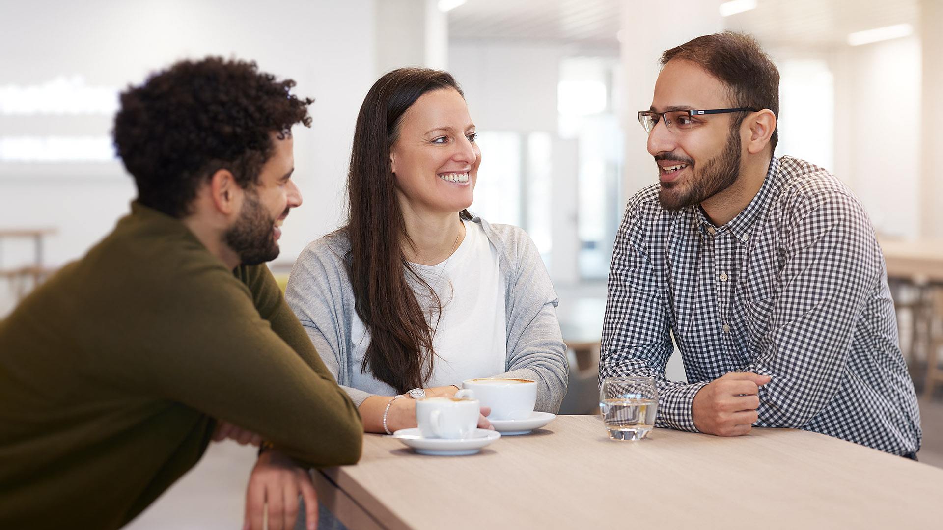 Drei ITK-Mitarbeiter die sich fröhlich unterhalten und Kaffee trinken.