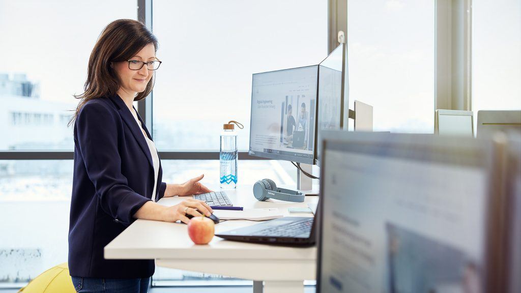 An ITK employee at a workstation with a height-adjustable table, provided with water and an apple