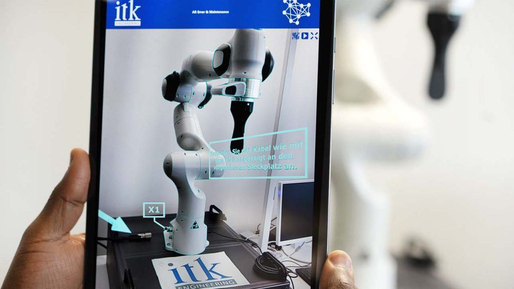 In der Hand gehaltenes Tablet mit Roboterarm auf dem Display sowie Fehlermeldungen für Servicetechniker über Augmented Reality.