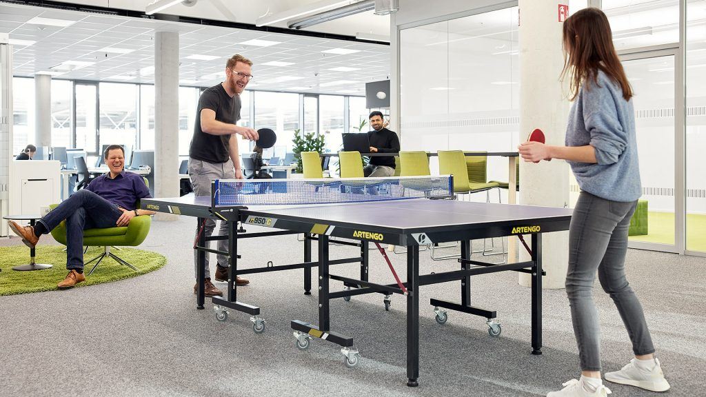 Mehrere ITK-Mitarbeiter im Aufenthaltsraum des Offices. Zwei Kollegen spielen Tischtennis