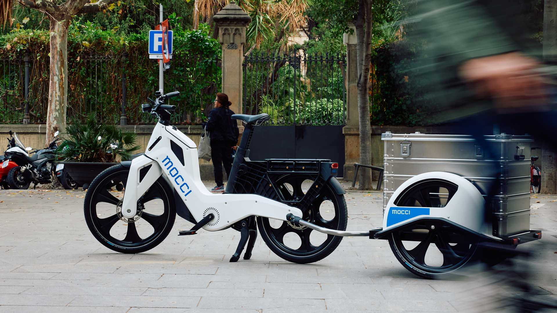 The e-bike mocci is parked in front of a park area.