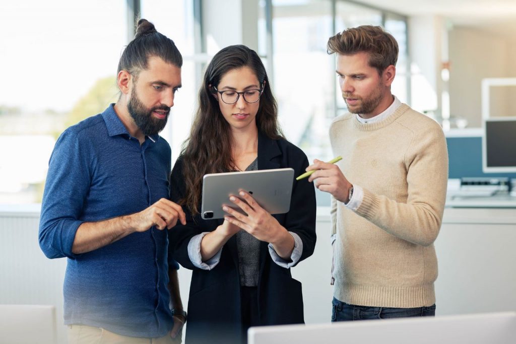 Drei ITK Kolleg:innen besprechen ein digitales Transformationsprojekt und legen die nächsten Schritte fest. In der Hand hält die Ingenieurin ein Tablet.