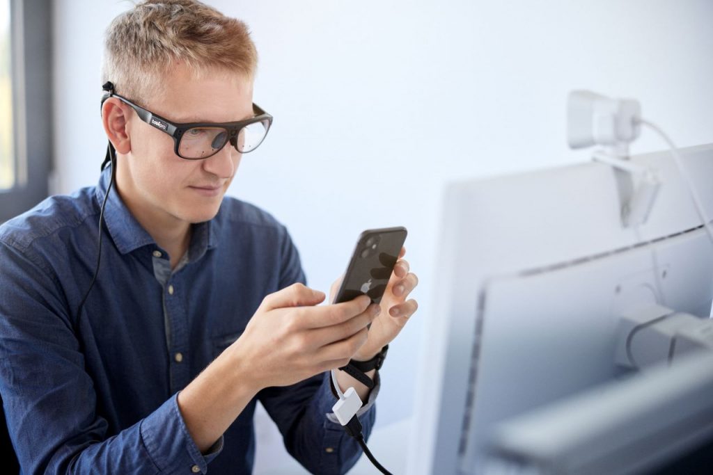 Ein Ingenieur trägt eine Eyetracking-Brille und blickt auf sein Smartphone.