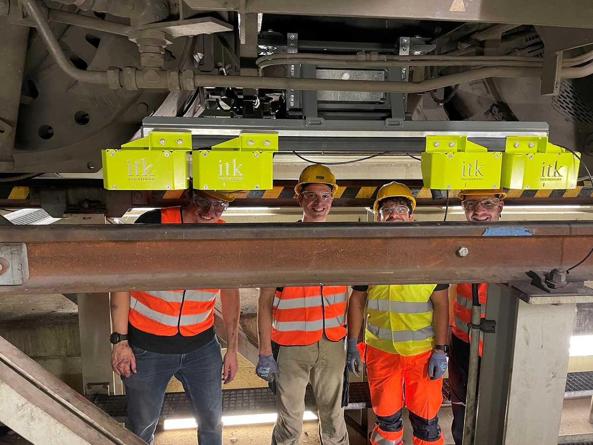 Experten von ITK und dem KIT stehen unter einer Lokomotive hinter dem installierten MAROS-Sensor