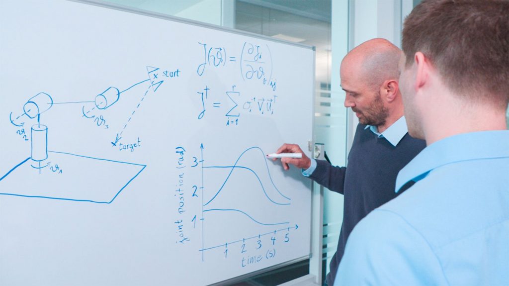 Zwei Ingenieure berechnen die Bewegungen eines Roboterarms an einem Whiteboard.