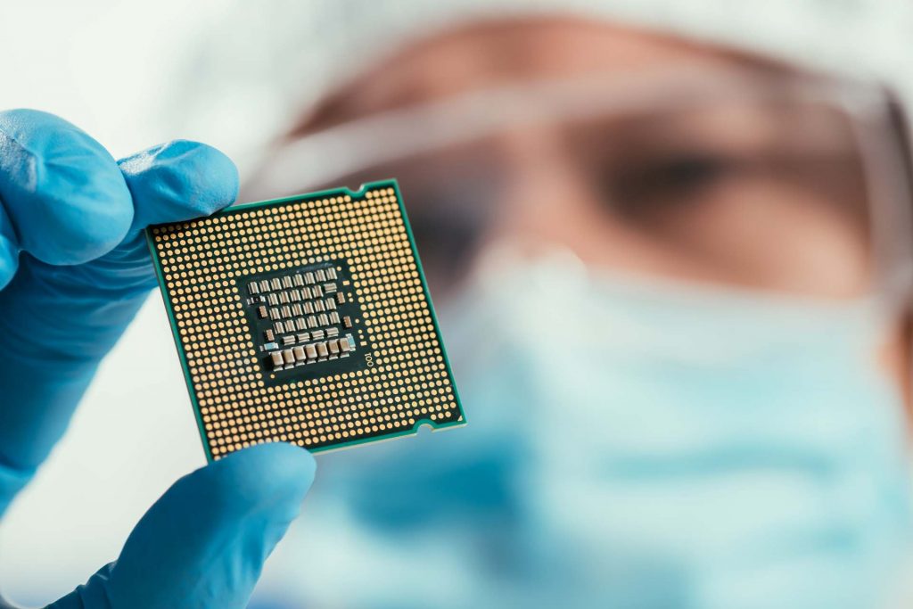 Eine Person mit blauem Handschuh hält einen Computerprozessor – ITK unterstützt bei der Integration von Mikrocontroller- und SoC/SoM-Lösungen und optimiert Entwicklungs-, Produktions- und Prüfprozesse.