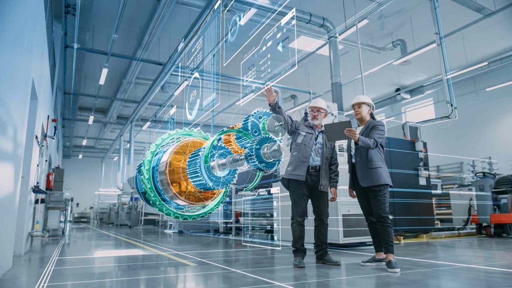 Zwei Personen in einer Fabrikumgebung bedienen einen digitalen Bildschirm mit Betriebsinformationen – ein Beispiel für die Anwendung digitaler Komponenten und IoT-Systeme, die ITK für die Industrie entwickelt.