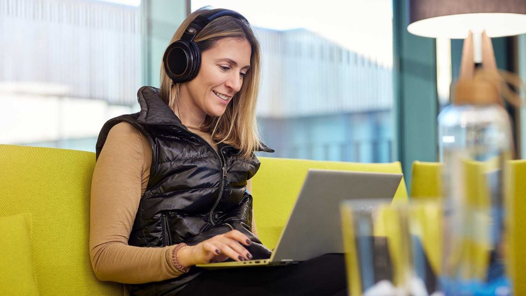 A woman sits on a green couch wearing headphones and watches a recorded webinar from the ITK media library.