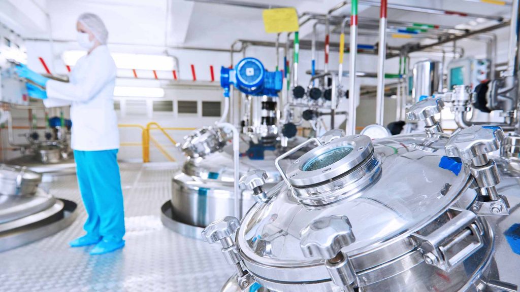 A woman in a lab coat stands in front of a large stainless steel machine.