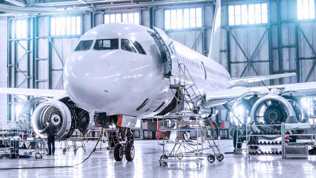 An aircraft is being serviced in a hangar. Technicians are busy inspecting and repairing it.