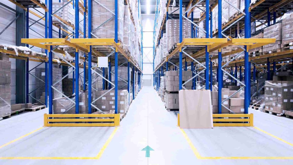 A warehouse with high shelves and a blue arrow pointing straight ahead into the aisle.